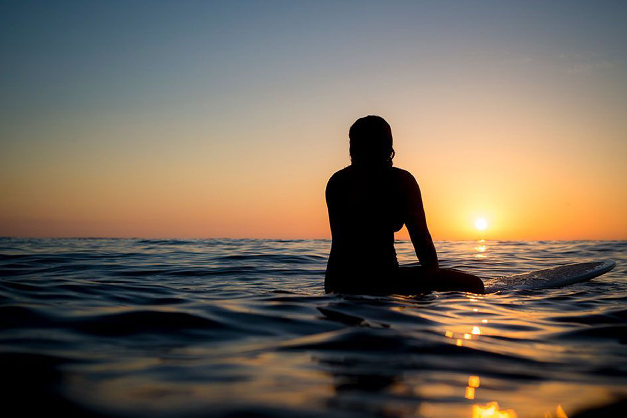 Person sits on surfboard in ocean