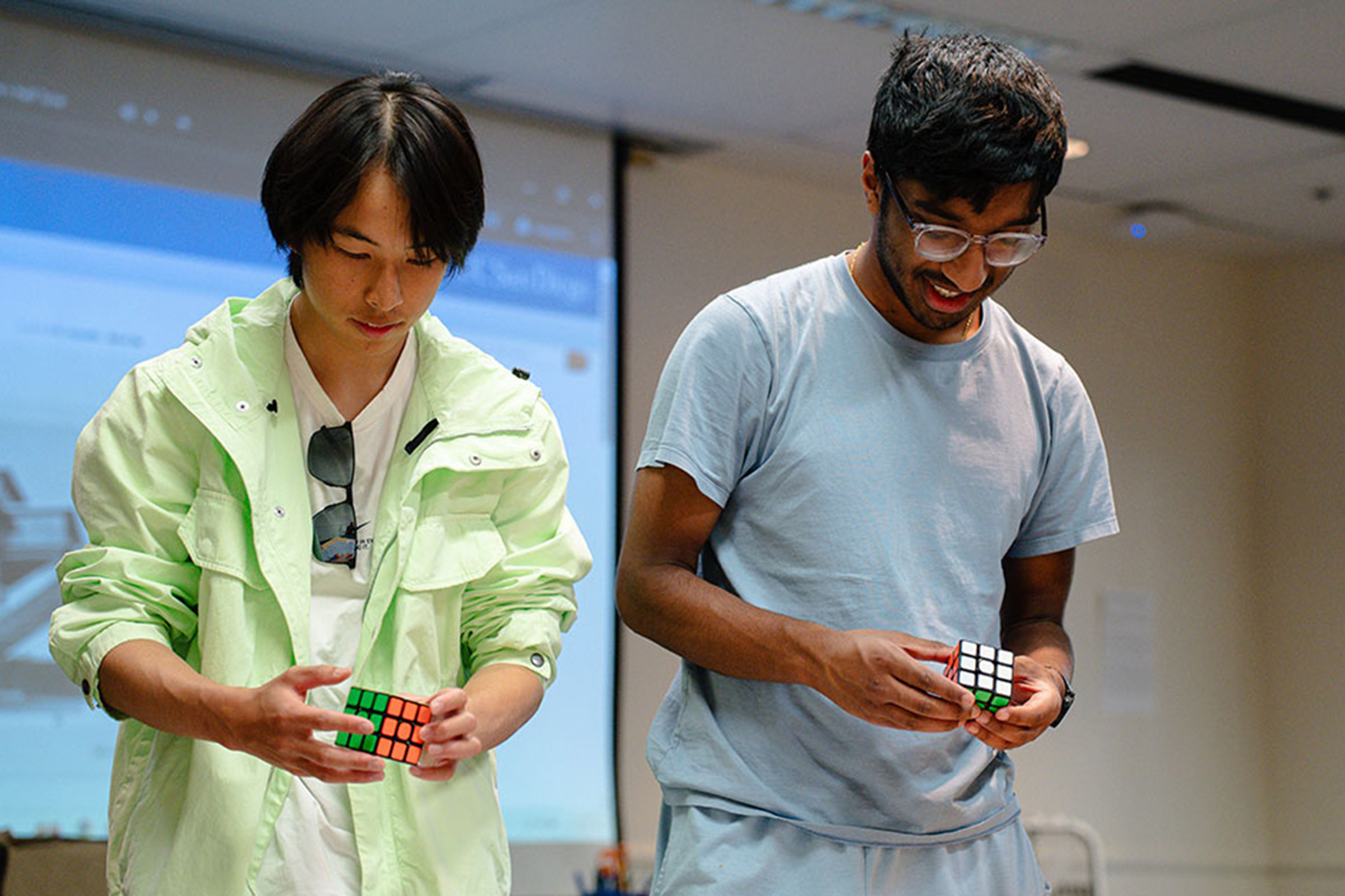 Two students stand up while solving Rubik's cube.